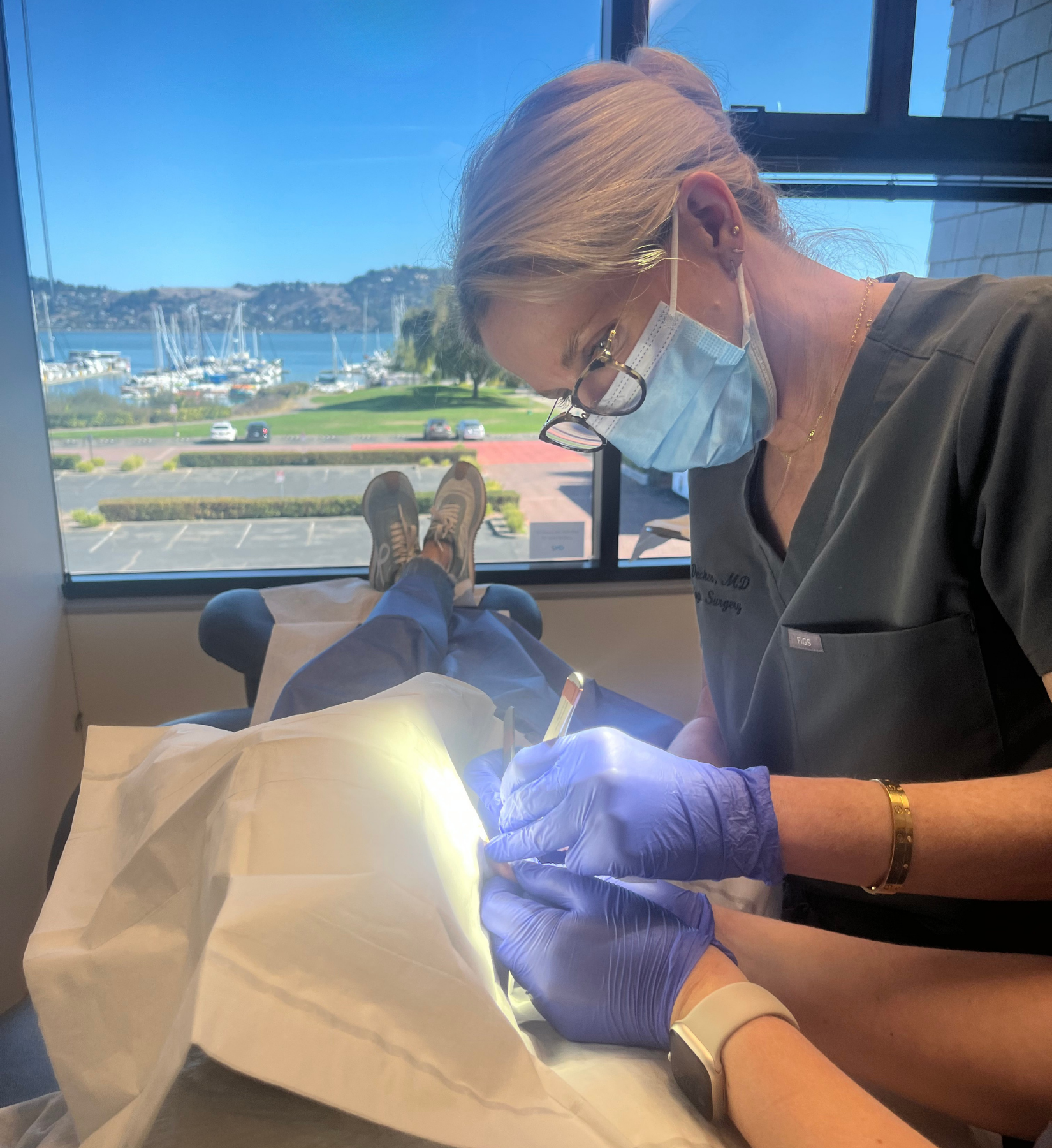 Dr. Ashley Decker performing precise Mohs surgery in a serene treatment room, with stunning views of Richardson Bay in the background.