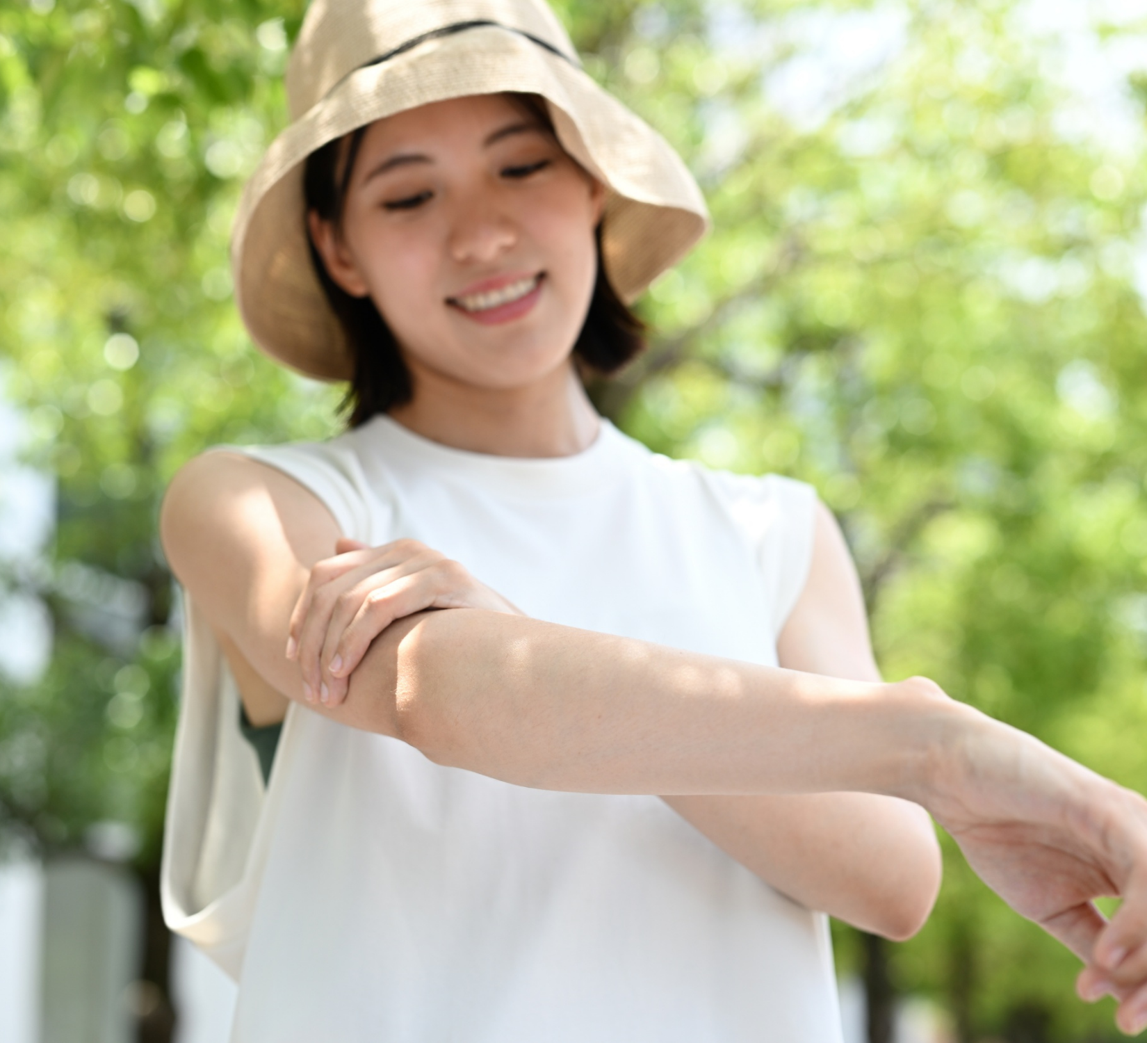 A woman wearing a sun hat and applying broad-spectrum sunscreen to protect her skin from harmful UV rays during an outdoor activity.